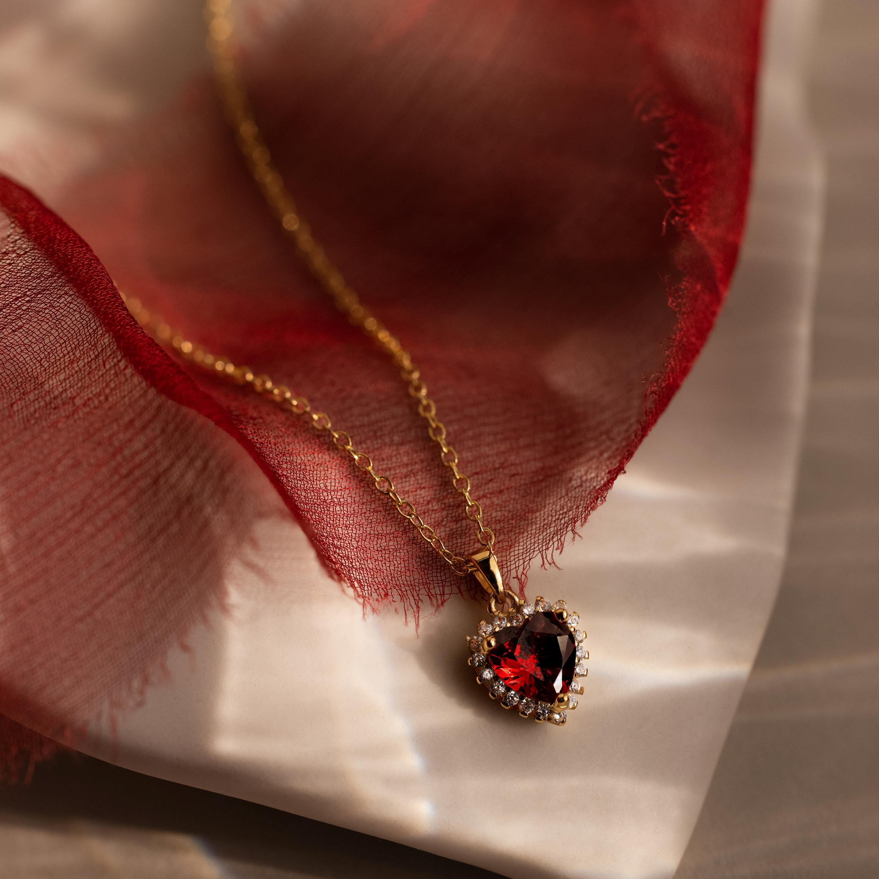Elegant pave heart necklace featuring a deep red garnet center on a delicate gold chain.